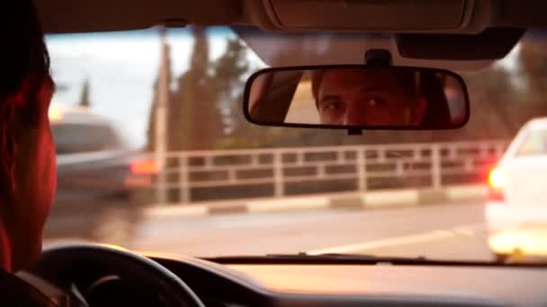 Spiegelung des Fahrers des Mannes im Rückspiegel. Ein Mann fährt mit einem Auto durch die Abendstadt. 4k, Hintergrund verschwommen. — Stockvideo