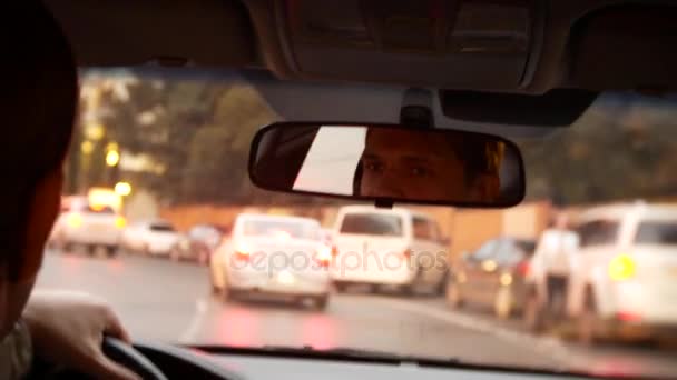 Reflectie van de bestuurder van de man in de achteruitkijkspiegel. een man rijdt een auto rond de stad 's avonds. 4k, achtergrond vervagen. — Stockvideo