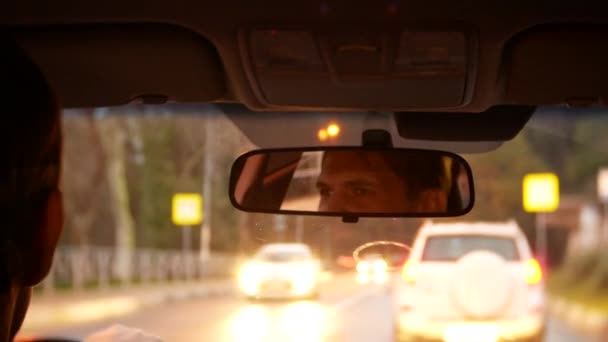 Reflejo del conductor del hombre en el espejo retrovisor. Un hombre conduce un coche por la ciudad nocturna. 4k, desenfoque de fondo . — Vídeo de stock