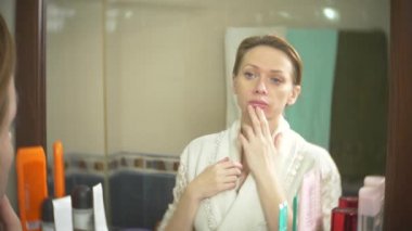 Orta yaşlı bir kadın cildi bir ayna önünde bakarak. kadının yüzündeki kırışıklıklar görünüyor. 4k, ağır çekim