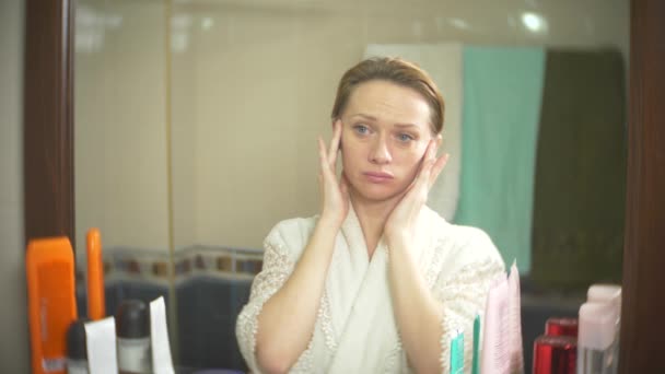 Femme d'âge moyen regardant sa peau devant un miroir. femme regarde les rides sur son visage. 4k, au ralenti — Video