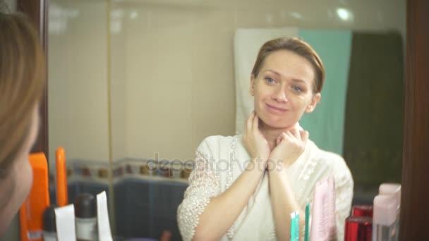 Middelbare leeftijd vrouw die haar huid in een spiegel kijkt. vrouw zoekt rimpels op haar gezicht. 4k, slow-motion — Stockvideo