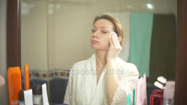 Жінка очищає обличчя ватним тампоном перед дзеркалом. 4k, повільний рух. крупним планом. розмиття тла . — стокове відео