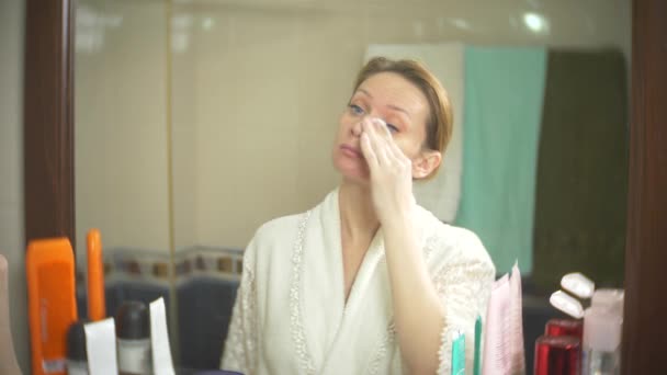 Женщина моет лицо ватным тампоном перед зеркалом. 4К, замедленная съемка. крупным планом. Фоновое размытие . — стоковое видео