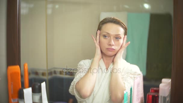 Femme d'âge moyen regardant sa peau devant un miroir. femme regarde les rides sur son visage. 4k, au ralenti — Video