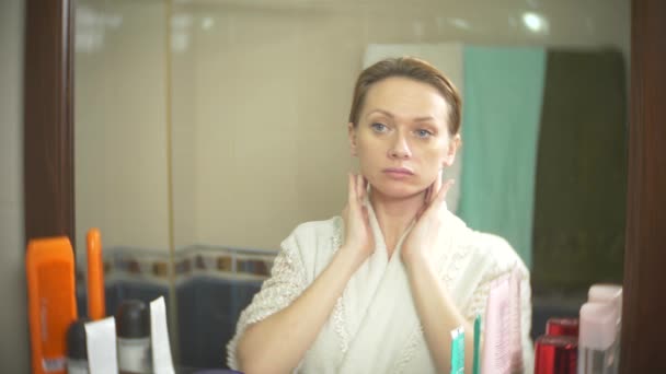 Femme d'âge moyen regardant sa peau devant un miroir. femme regarde les rides sur son visage. 4k, au ralenti — Video