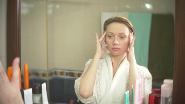 Kobieta w średnim wieku patrząc na jej skórę przed lustrem. kobieta wygląda zmarszczek na twarzy. 4k, zwolnionym tempie — Wideo stockowe