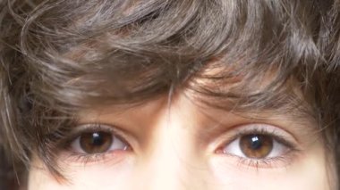 Siyah uzun kirpik bir çocukla kahverengi gözleri. uzun kıvırcık kâkül altından görünüyor. 4 k, ağır çekim, yakın çekim