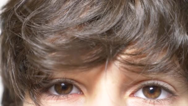 Brązowe oczy chłopca z długie, czarne rzęsy. on wygląda spod długie kręcone Kosmyk. 4 k, zwolnionym tempie, zbliżenie — Wideo stockowe