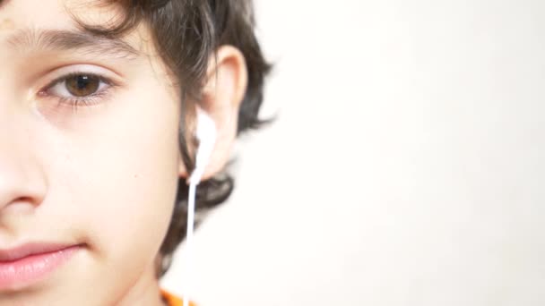 Tonåringen sätter på vita hörlurar och lyssnar på musik. närbild på halv ett ansikte. Kopiera utrymme. 4k, Slowmotion — Stockvideo
