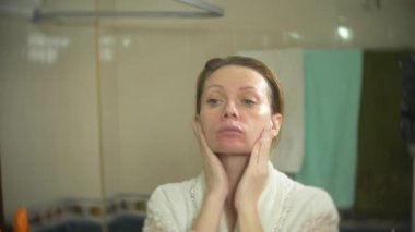 yüz ve boyun banyoda krem uygulayarak bornoz kadında. 4k, ağır çekim