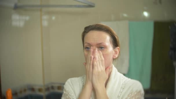 Femme en peignoir appliquer la crème sur le visage et le cou dans la salle de bain. 4k, au ralenti — Video