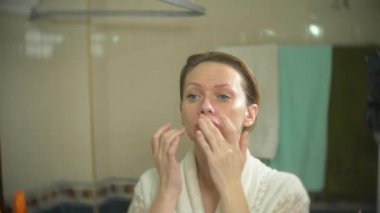 yüz ve boyun banyoda krem uygulayarak bornoz kadında. 4k, ağır çekim