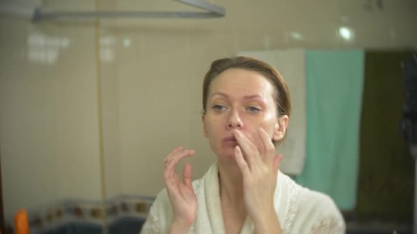 Femme en peignoir appliquer la crème sur le visage et le cou dans la salle de bain. 4k, au ralenti — Video