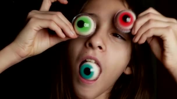 Gros plan. une adolescente joyeuse apporte un gros bonbon rond à ses yeux, semblable à des yeux. 4k . — Video