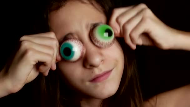 Primer plano. una adolescente alegre trae un gran caramelo redondo a sus ojos, similar a los ojos. 4k . — Vídeo de stock