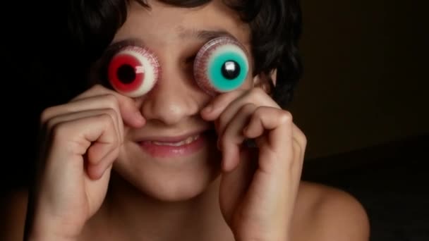 Γκρο πλαν. Ένα χαρούμενο εφηβικό αγόρι φέρνει το μεγάλο στρογγυλό καραμέλα ματιών, παρόμοια με τα μάτια. 4k. — Αρχείο Βίντεο