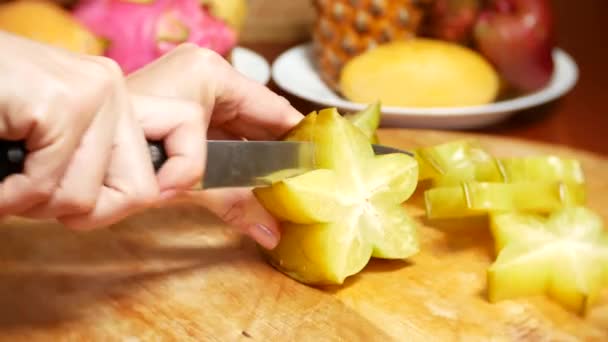 Εξωτικά φρούτα στο τραπέζι. 4k, γυναικεία χέρια κόβουμε ένα καράμβολες με ένα μαχαίρι σε ένα ξύλο κοπής — Αρχείο Βίντεο