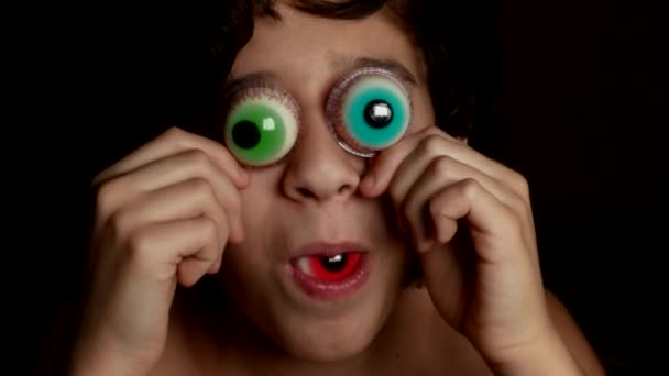 Primer plano. Un adolescente alegre trae a los ojos grandes caramelos redondos, similares a los ojos. 4k . — Vídeo de stock