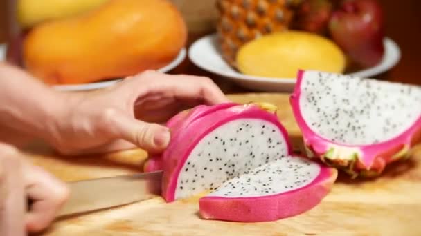 Egzotycznych owoców na stole. 4k, kobiecych rąk cięcia dragonfruit z nożem na deska do krojenia na kawałki — Wideo stockowe