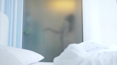 4k, ağır çekim. Tanınmayan kız duş alır. biri yatak odası ve banyo arasında şeffaf duvarı baktığı. Bulanık cam arkasındaki kadın. Kadın banyoda.