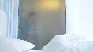 4k, ağır çekim. Tanınmayan kız duş alır. biri yatak odası ve banyo arasında şeffaf duvarı baktığı. Bulanık cam arkasındaki kadın. Kadın banyoda.