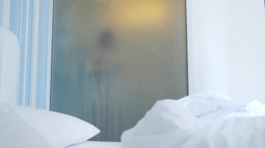 4k, ağır çekim. Tanınmayan kız duş alır. biri yatak odası ve banyo arasında şeffaf duvarı baktığı. Bulanık cam arkasındaki kadın. Kadın banyoda.