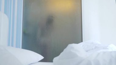 4k, ağır çekim. Tanınmayan kız duş alır. biri yatak odası ve banyo arasında şeffaf duvarı baktığı. Bulanık cam arkasındaki kadın. Kadın banyoda.