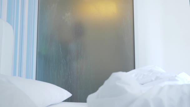 4k, au ralenti. fille méconnaissable prend une douche. quelqu'un le regarde à travers le mur transparent entre la chambre et la salle de bain. La femme derrière le verre flou. Femme dans la salle de bain . — Video