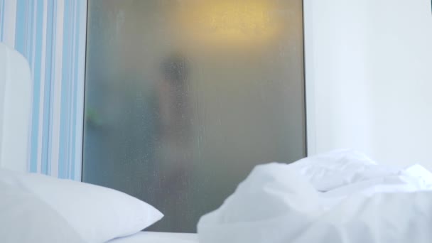 4k, rallenta. ragazza irriconoscibile si fa una doccia. qualcuno lo guarda attraverso il muro trasparente tra la camera da letto e il bagno. La donna dietro il vetro sfocato. Donna in bagno . — Video Stock