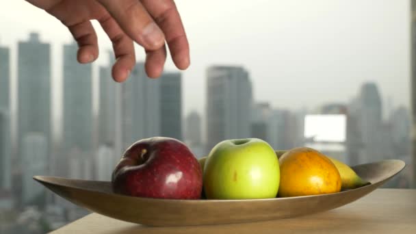 La mano toma la manzana del plato, contra la ventana con una vista de los rascacielos. 4k, cámara lenta — Vídeo de stock