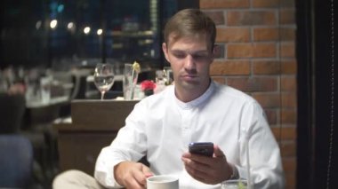 bir kişi bir cep telefonu bir restoranda geceleri kontrol kahve, içecekler. 4k, arka plan bulanıklık