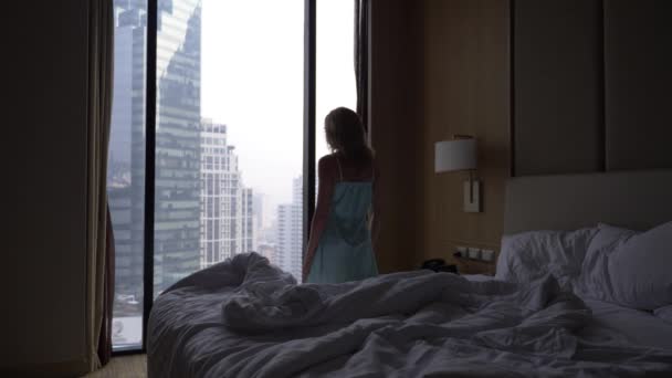 The woman wakes up from sleep and comes to the window with a view of the skyscrapers, slow movement. 4k — Stock Video