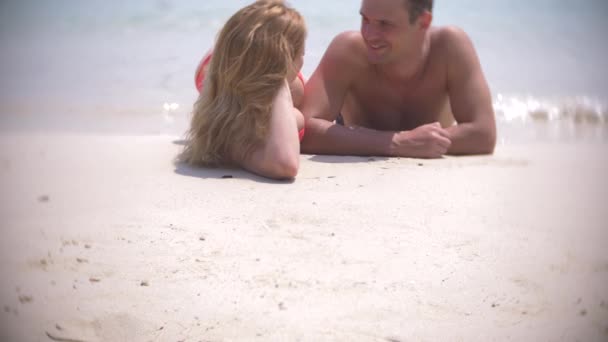 Пара влюбленных лежат на песке на пляже и целуются, в ясный солнечный день. 4k, slow motion — стоковое видео