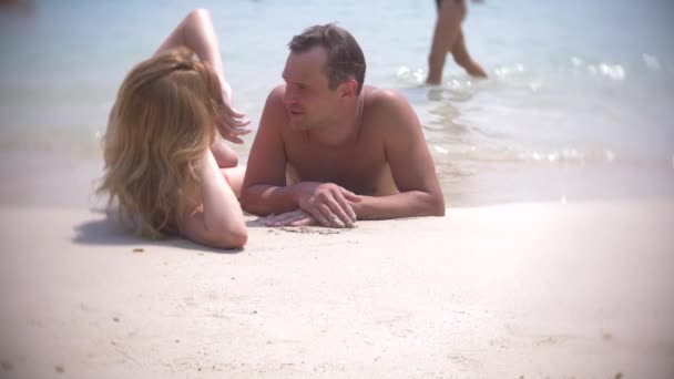 Een paar liefhebbers liggen op het zand op het strand en de kus, op een heldere zonnige dag. 4k, slow-motion — Stockvideo
