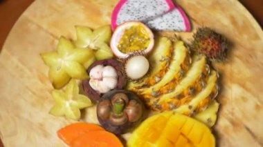 egzotik meyveler masanın üzerinde. 4k, üstten görünüm, ağır çekim. carambola ve dragon meyve, papaya, mango, mangosten ve longan, tutku meyve, meyve kesilmiş parçalar halinde bir ananas kesme tahtası üzerinde döndürme.