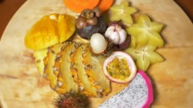 egzotik meyveler masanın üzerinde. 4k, üstten görünüm, ağır çekim. carambola ve dragon meyve, papaya, mango, mangosten ve longan, tutku meyve, meyve kesilmiş parçalar halinde bir ananas kesme tahtası üzerinde döndürme.