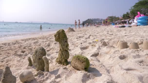 Castillo de arena en la playa, coral expulsado por el mar a la orilla, una familia irreconocible pasea por una playa pública. 4k, desenfoque, desaceleración — Vídeo de stock