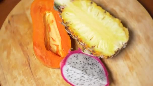 Exotische vruchten op de tafel. 4k, bovenaanzicht, slow-motion. Dragon fruit, papaya, ananas, gehakt, draaien op een snijplank. — Stockvideo