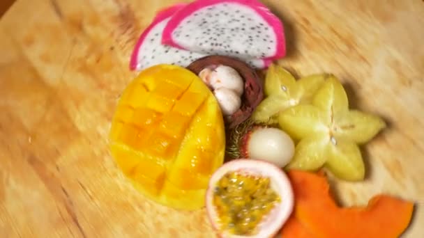 Exotic fruits on the table. 4k, top view, slow motion. carambola and dragon fruit, papaya, mango, mangosteen and longan, passion fruit, fruit cut into pieces, rotate on a cutting board — Stock Video