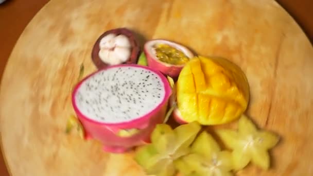 Fruits exotiques sur la table. 4k, vue du dessus, ralenti. caramboles et fruits du dragon, papaye, mangue, mangoustan et longan, fruits de la passion, fruits coupés en morceaux, tourner sur une planche à découper — Video