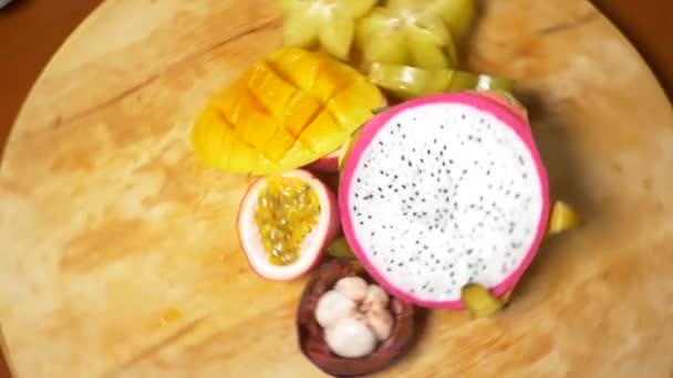 Exotische Früchte auf dem Tisch. 4k, Draufsicht, Zeitlupe. Karambola- und Drachenfrüchte, Papaya, Mango, Mangostan und Longan, Passionsfrucht, Früchte in Stücke schneiden, auf einem Schneidebrett drehen — Stockvideo