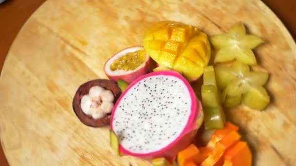 Экзотические фрукты на столе. 4К, вид сверху, замедленная съемка. карамбола и дракон фрукты, папайя, манго, мангостин и Лонган, маракуйя фрукты, разрезанные на куски, вращаются на разделочной доске — стоковое видео