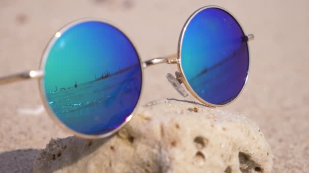 A homok a tengerparton fekvő napszemüveg. A napszemüveg tükrözik a tenger, a nap, az ég, a strandon. 4k, lassú mozgás — Stock videók