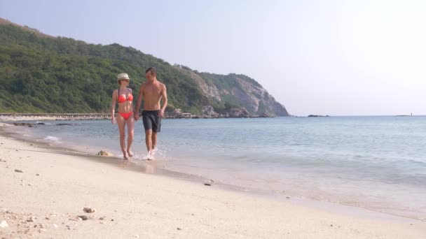 Bir çift sahilde, eller, bir erkek ve bir kadın tutarak yürüyor. Turistler denizde dinleniyor. Ağır çekim, 4k — Stok video