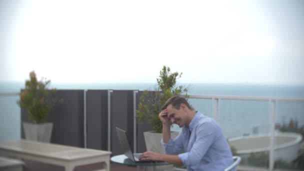 Бізнесмен з ноутбуком біля басейну на даху з видом на море. 4k. , розмити фон — стокове відео