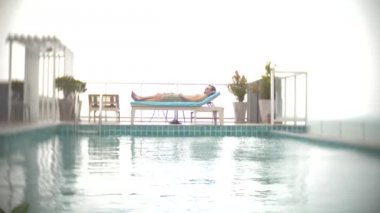 Rahatlatıcı, Deniz Manzaralı Çatıda havuz kenarında şezlong üzerinde güneşlenmek bir adam. 4k, arka plan bulanıklık