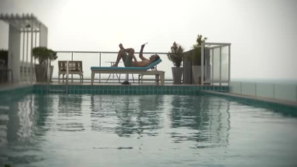Молодой человек с табличкой у бассейна на крыше с видом на море. 4k. , размыть фон — стоковое видео