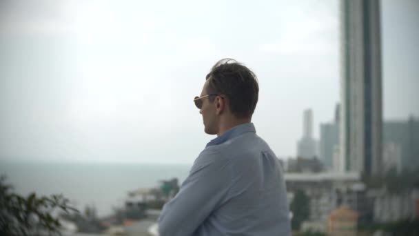 Un uomo guardando in lontananza, in piedi sulla terrazza con vista sul mare. 4k, sfocatura dello sfondo — Video Stock