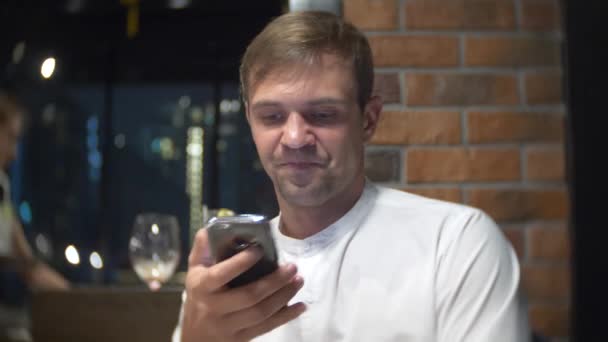 Man kontrollerar en mobiltelefon på natten i en restaurang. 4k, bakgrundsoskärpa — Stockvideo